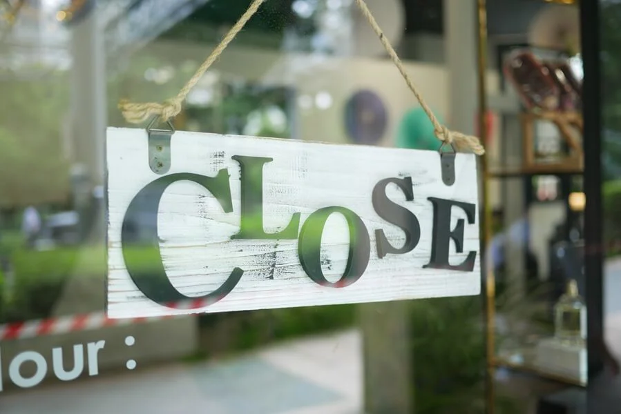 A closed sign on a shop door reflecting greenery.